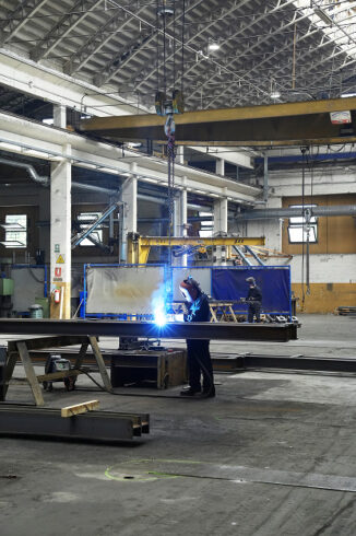 Saldatore STAM al lavoro su un grande telaio metallico nel reparto attrezzato con gru a ponte